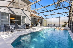 Una piscina interior con techo de vidrio, sillas de descanso y una parrilla de barbacoa.