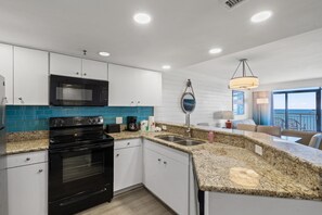A modern kitchen with white cabinets, a black oven, a microwave, and a granite countertop. - Stay Above the Sea! 3BR Oceanview Penthouse in uptown Myrtle Beach (Myrtle Beach)