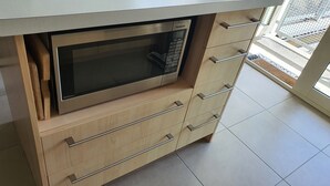 A kitchen with a built-in microwave, wooden cabinetry, and a tiled floor. - Arrowtown Central Apartment with Sundeck (Arrowtown)