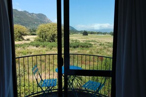 A balcony with a table and two chairs, overlooking a grassy field and mountains. - Pohara Escape - Bright Interiors & Scenic Views (Pōhara)