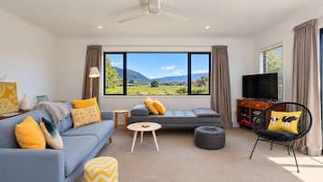 A modern living room with a sofa, ottoman, and a chair, a television, and a large window with a mountain view.