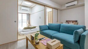 Ein modernes Wohnzimmer mit einem blauen Sofa, einem Couchtisch mit Pflanze, Fernbedienungen und einem kleinen Bücherregal.