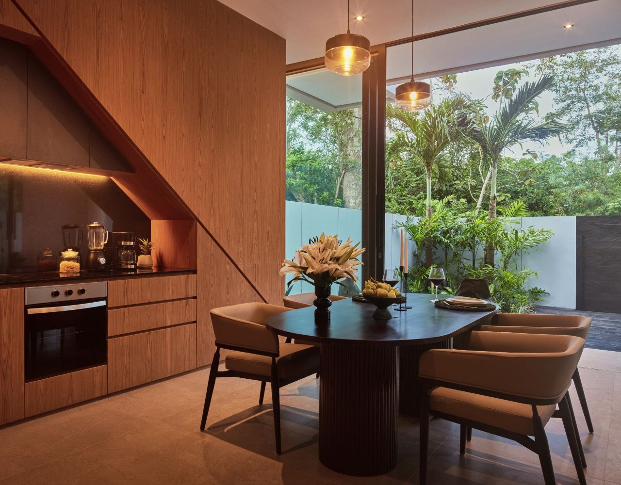 A modern kitchen with wooden cabinetry, a dining table with chairs, and a view of lush greenery outside.