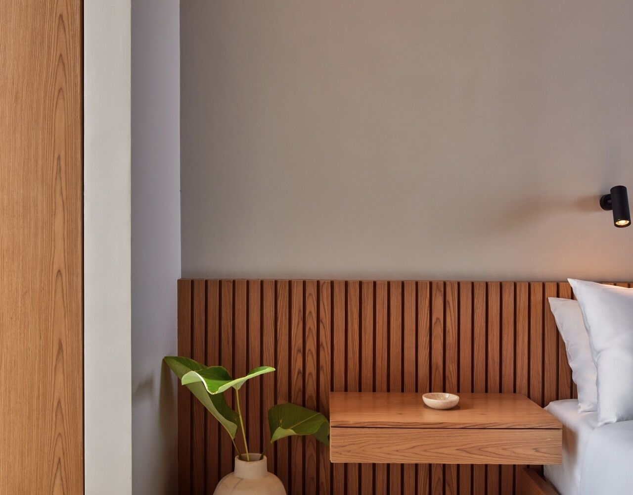 A room with a wooden slat wall, a small wooden table with a bowl, a vase with a plant, and a white pillow.