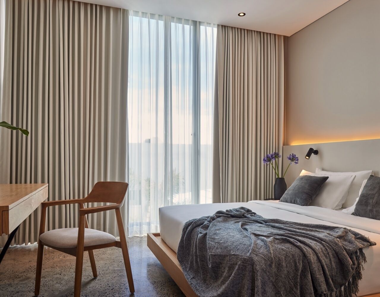 A modern hotel room with a large bed, a desk, and a chair.