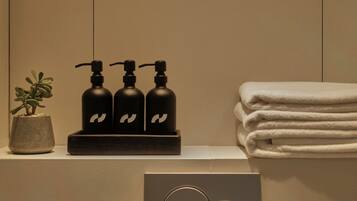 A bathroom with a sink, three black soap dispensers, a potted plant, and a stack of white towels.