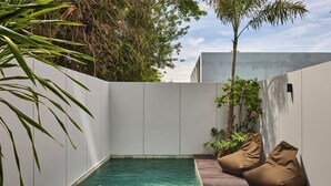 Une piscine avec une terrasse en bois et des fauteuils en forme de sac de haricots.