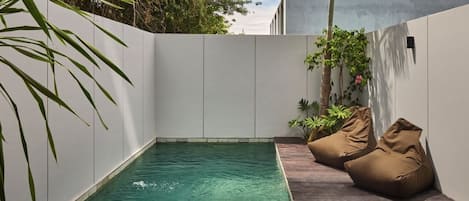 A swimming pool with a wooden deck and bean bag chairs.