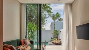 Un salon moderne avec un canapé vert, une table basse et une vue sur une piscine et la verdure environnante.