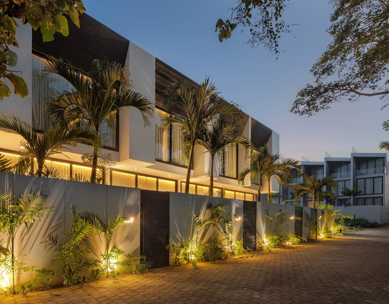A modern building with a paved courtyard, palm trees, and a well-lit entrance.