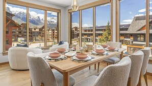 Comedor con una mesa grande dispuesta para seis personas, ventanas amplias que ofrecen vistas a la montaña y una lámpara moderna.