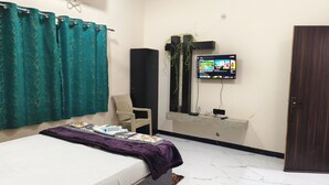 Una camera da letto con un letto, una sedia, un televisore e una porta.