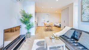 A modern living room with a flat-screen TV, a sofa, a dining table, and a potted plant. - StayAU Convenient City Apt in West Melb (West Melbourne)