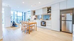 A modern kitchen with white cabinetry, a stainless steel refrigerator, and a dining area with wooden chairs and a table. - StayAU Convenient City Apt in West Melb (West Melbourne)