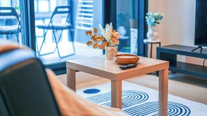 A modern living room with a wooden coffee table, a vase with flowers, a remote control, and a television on a stand. - StayAU Convenient City Apt in West Melb (West Melbourne)