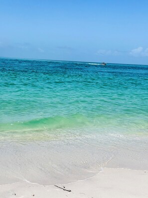 Ein Strand mit klarem türkisblauem Wasser, ein Boot in der Ferne und ein sandiger Uferstreifen.