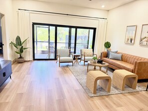 Ein großzügiger Wohnbereich mit einer Couch, Sesseln, einem Couchtisch und einer großen Glasschiebetür, die auf eine Terrasse im Freien führt.