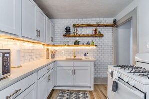 Cocina moderna con gabinetes blancos, estufa a gas y salpicadero de ladrillo.