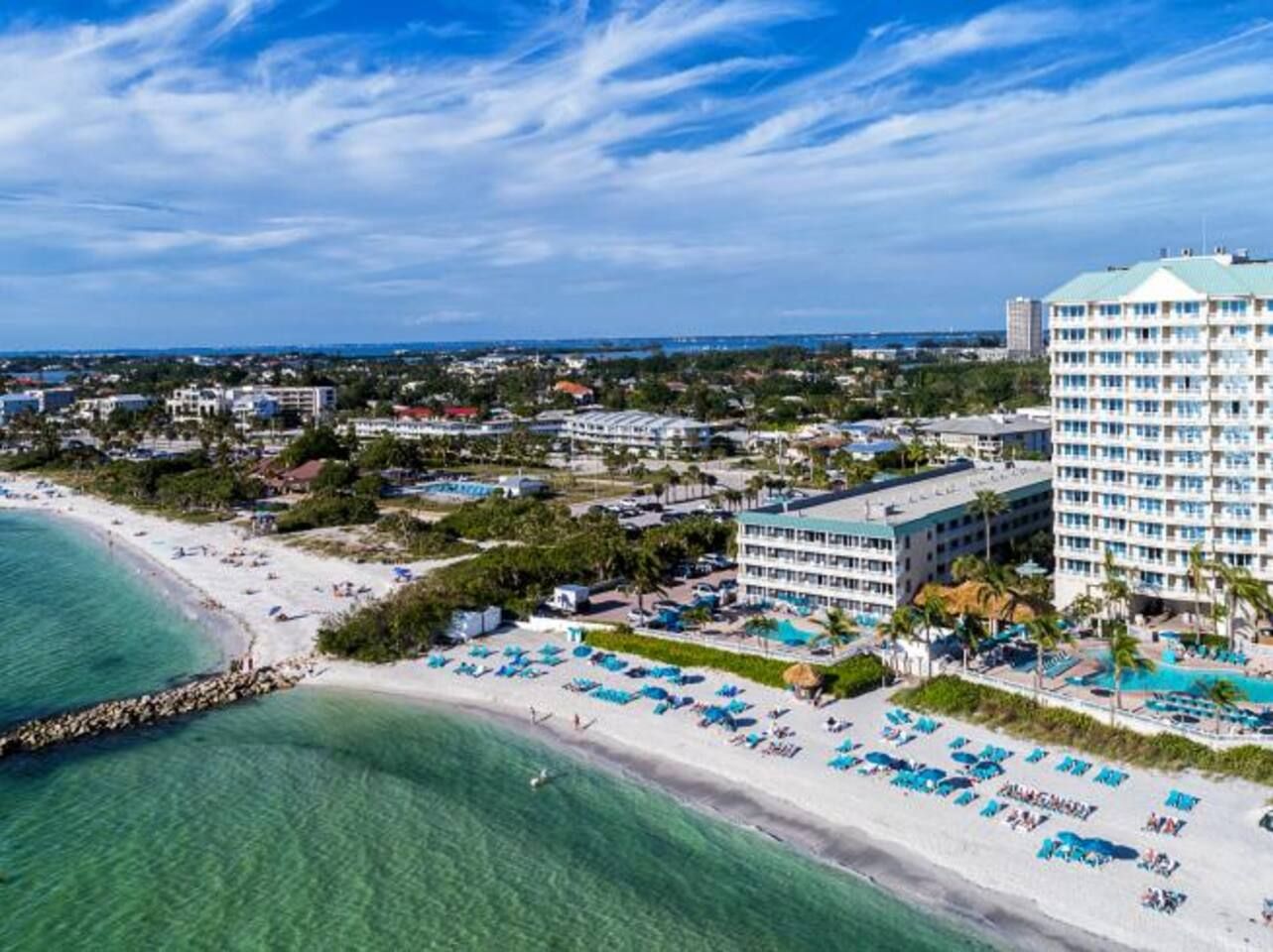 A coastal hotel with a beachfront, multiple swimming pools, and a large building with numerous balconies.