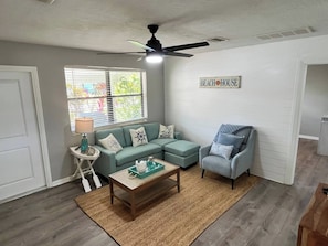 A living room with a ceiling fan, a sofa set, a coffee table, and a chair. - Ashota - The Driftwood (Sarasota)