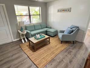 A living room with a sofa, armchair, coffee table, and a rug. - Ashota - The Driftwood (Sarasota)