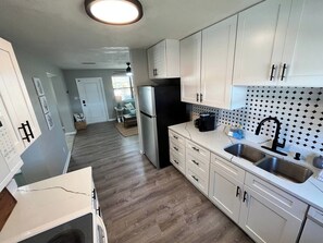 A kitchen with white cabinets, a black refrigerator, and a tiled backsplash. - Ashota - The Driftwood (Sarasota)