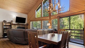 A spacious living area with a fireplace, a television, and a large window overlooking a forest.