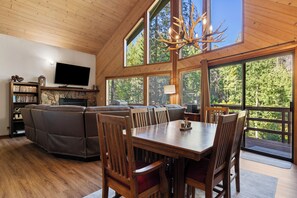 A spacious living area with a fireplace, a television, and a large window overlooking a forest.