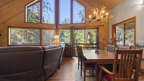 A wooden interior with a dining table, chairs, a sofa, and large windows.