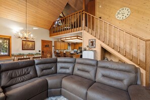 A spacious living area with a large sectional sofa, wooden staircase, and a kitchen in the background.