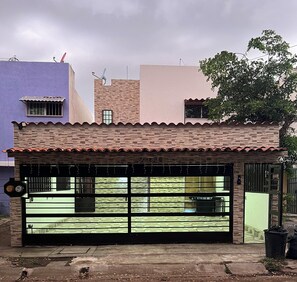 Un edifici residencial amb garatge, antena parabòlica i un arbre al fons.