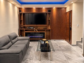 Ein Wohnzimmer mit Flachbildfernseher, Holzvertäfelung, einem grauen Sofa und einem Glastisch.