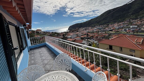 Un balcón con vistas a un pueblo costero, con piso de baldosas y barandillas blancas.