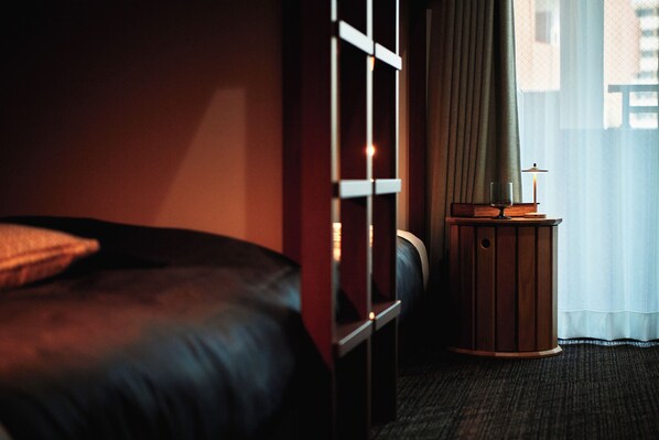 Een hotelkamer met een bed, een tafeltje met een lamp en een raam met gordijnen.