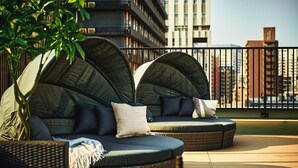 Une terrasse sur le toit dotée de deux espaces de détente semi-circulaires, chacun comprenant des coussins et une bouteille de vin.