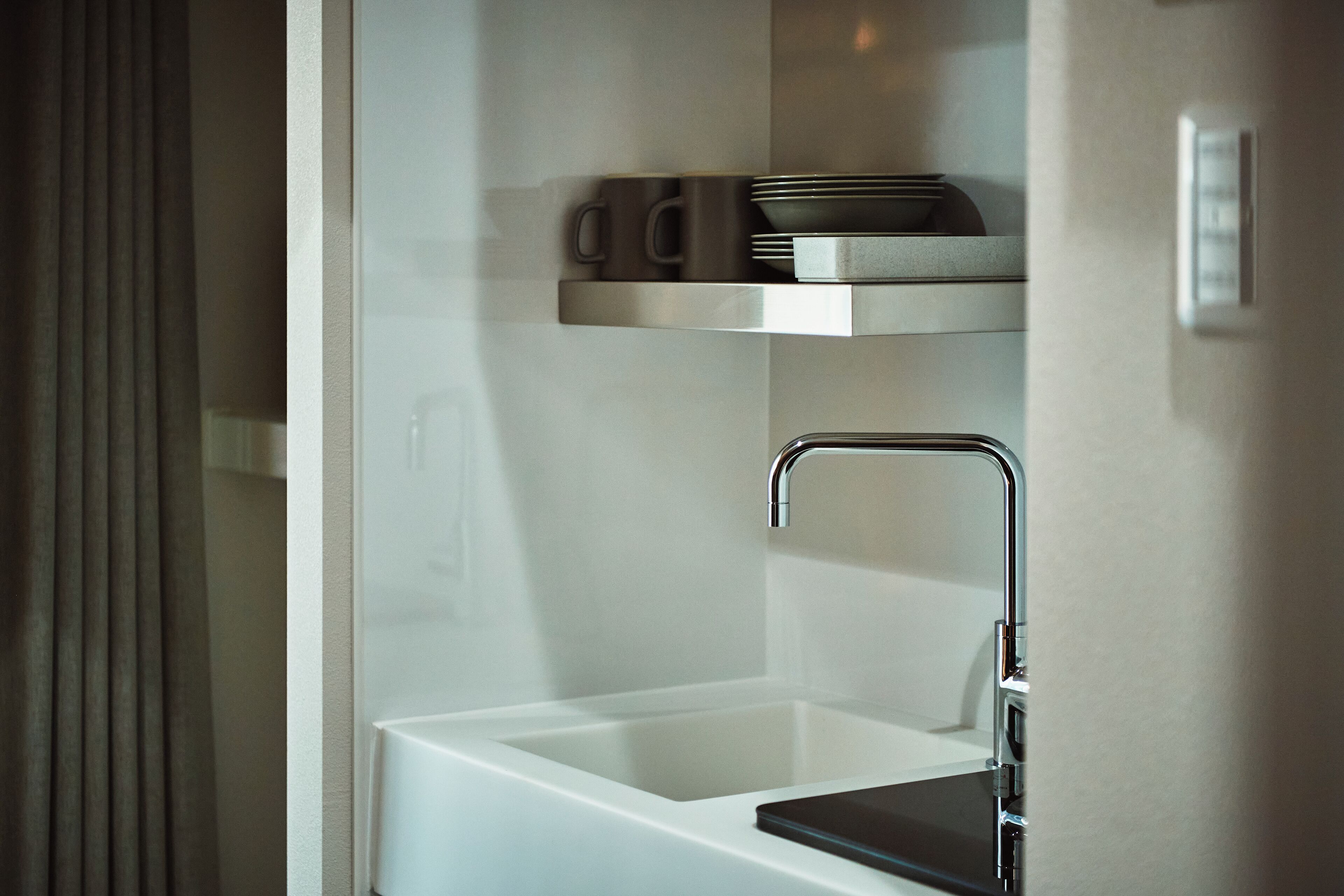 Un baño moderno con un lavabo blanco, un grifo cromado y un estante sobre el lavabo con una taza y un plato.
