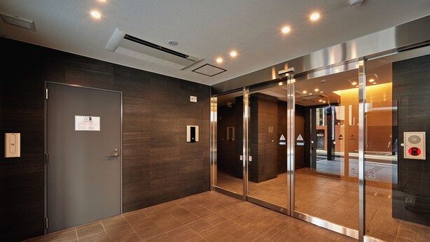 Un hall d’ascenseur moderne avec un mur en bois foncé, une porte en verre et un sol carrelé.