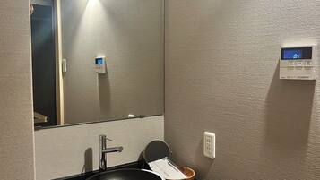 A modern bathroom with a black sink, a mirror, a wall-mounted digital clock, and a towel rack.