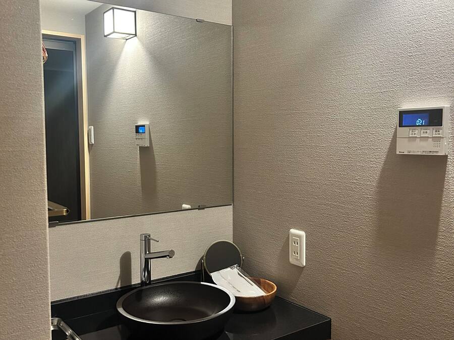 A modern bathroom with a black sink, a mirror, a wall-mounted digital clock, and a towel rack.