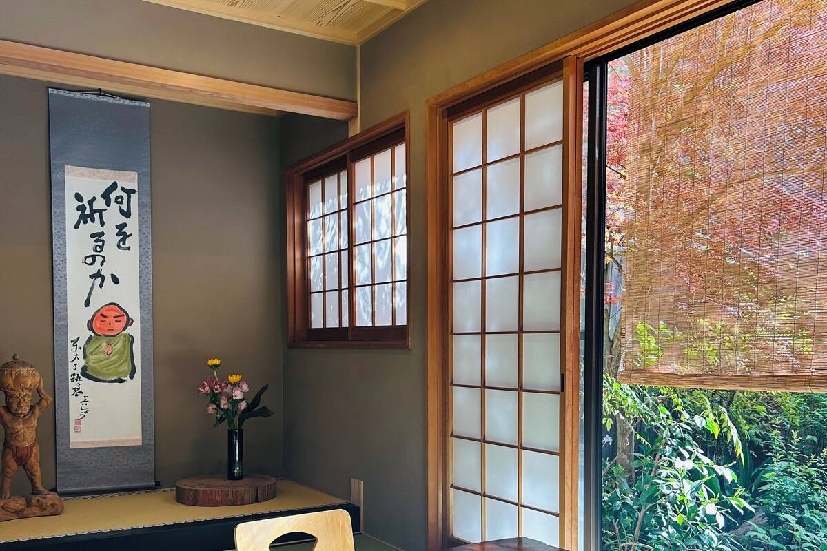 A tatami mat room with a low table, sliding doors, and a view of greenery.