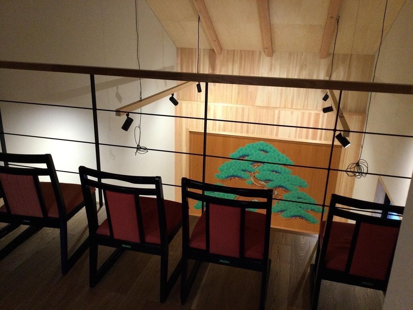 Une pièce avec un plafond en bois, un mur orné d’une fresque représentant un arbre vert et quatre chaises avec des coussins rouges.