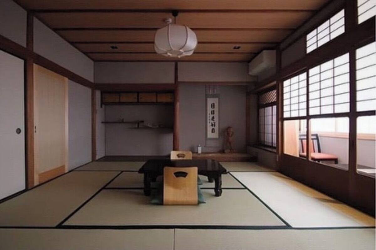 A traditional Japanese room with tatami flooring, a low table with a cushion, sliding doors, and a large window with a view.