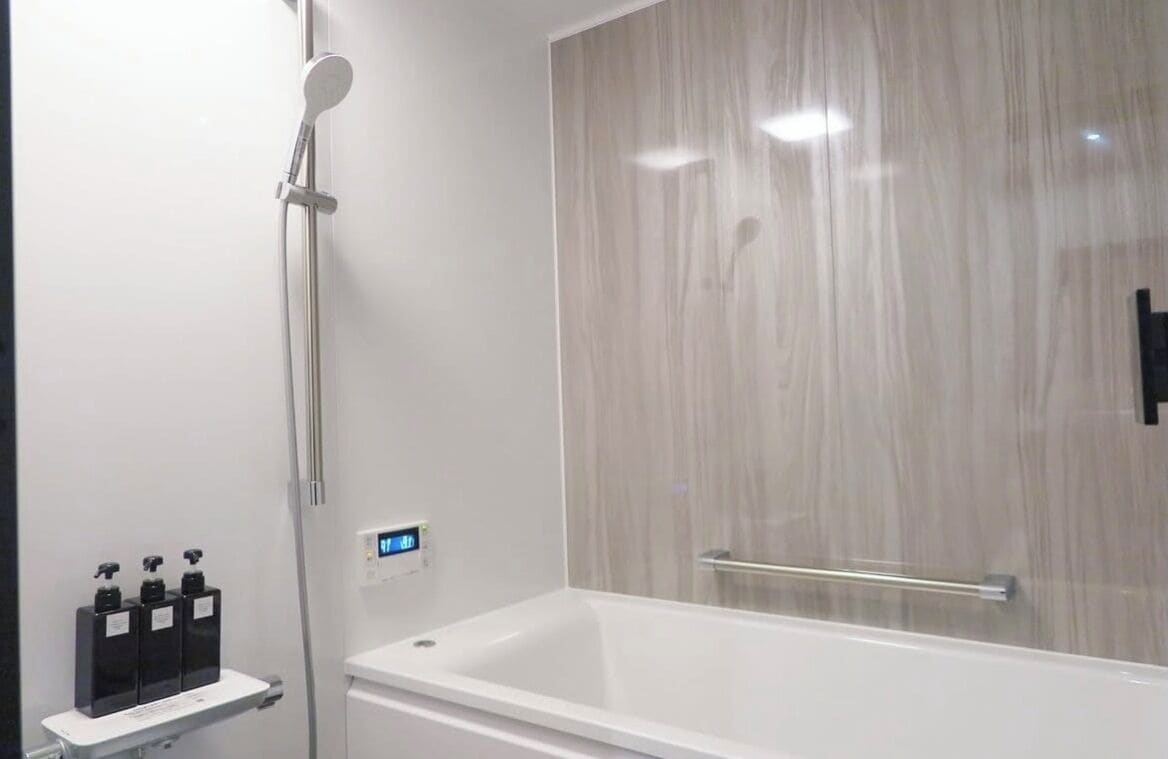 A modern bathroom with a white bathtub, a glass shower enclosure, and a wall-mounted soap dispenser.