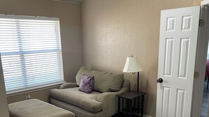 A room with a sofa, ottoman, lamp, and a door. - Kindness Dwells (Killeen)