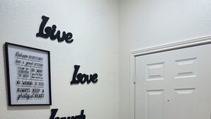 A hallway with a white door, a framed inspirational quote on the wall, and decorative wall art. - Kindness Dwells (Killeen)