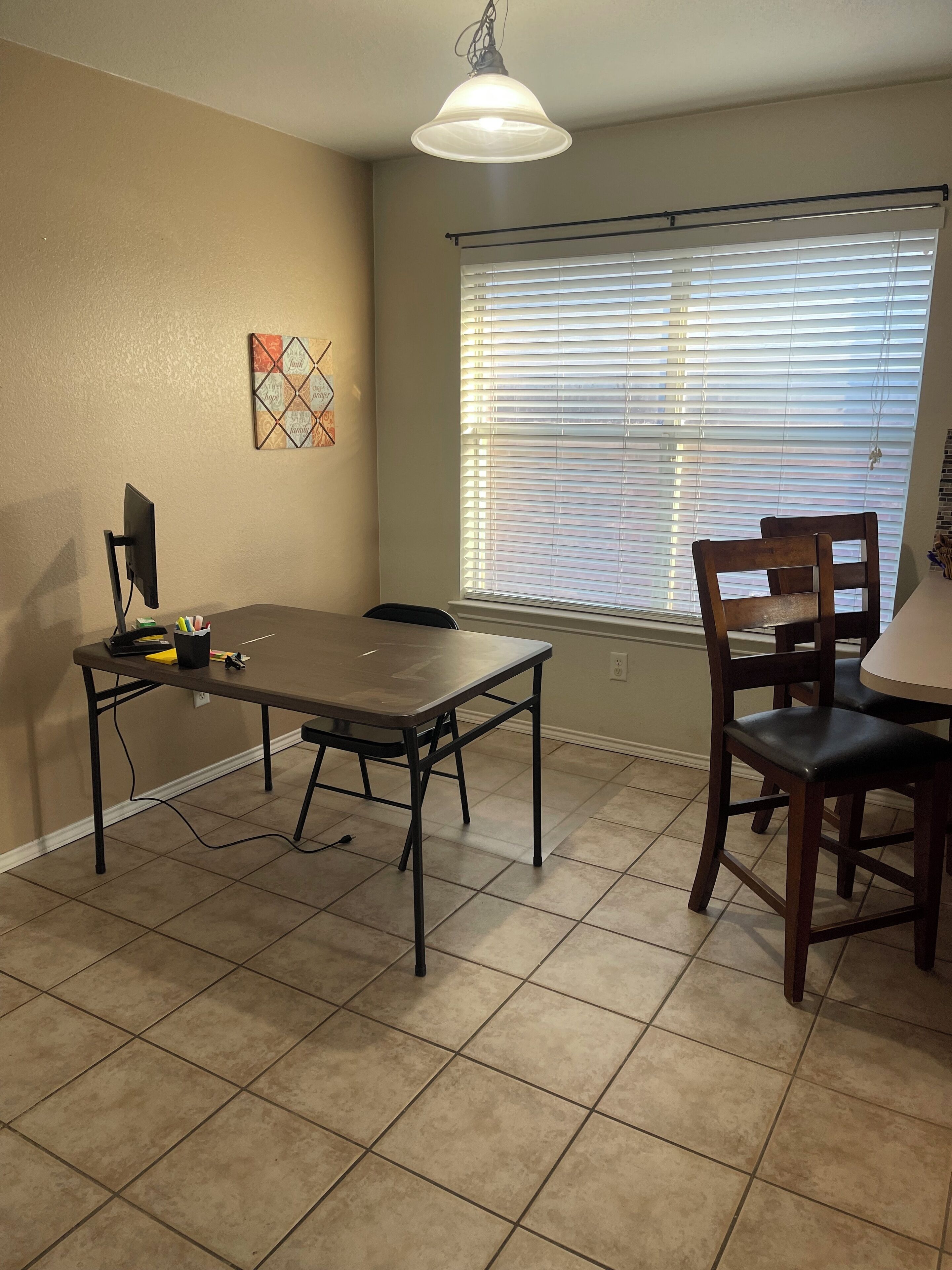 A dining area with a table, chairs, a computer, and a window with blinds.