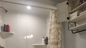 Un bany amb banyera, vàter i prestatges amb articles de tocador.