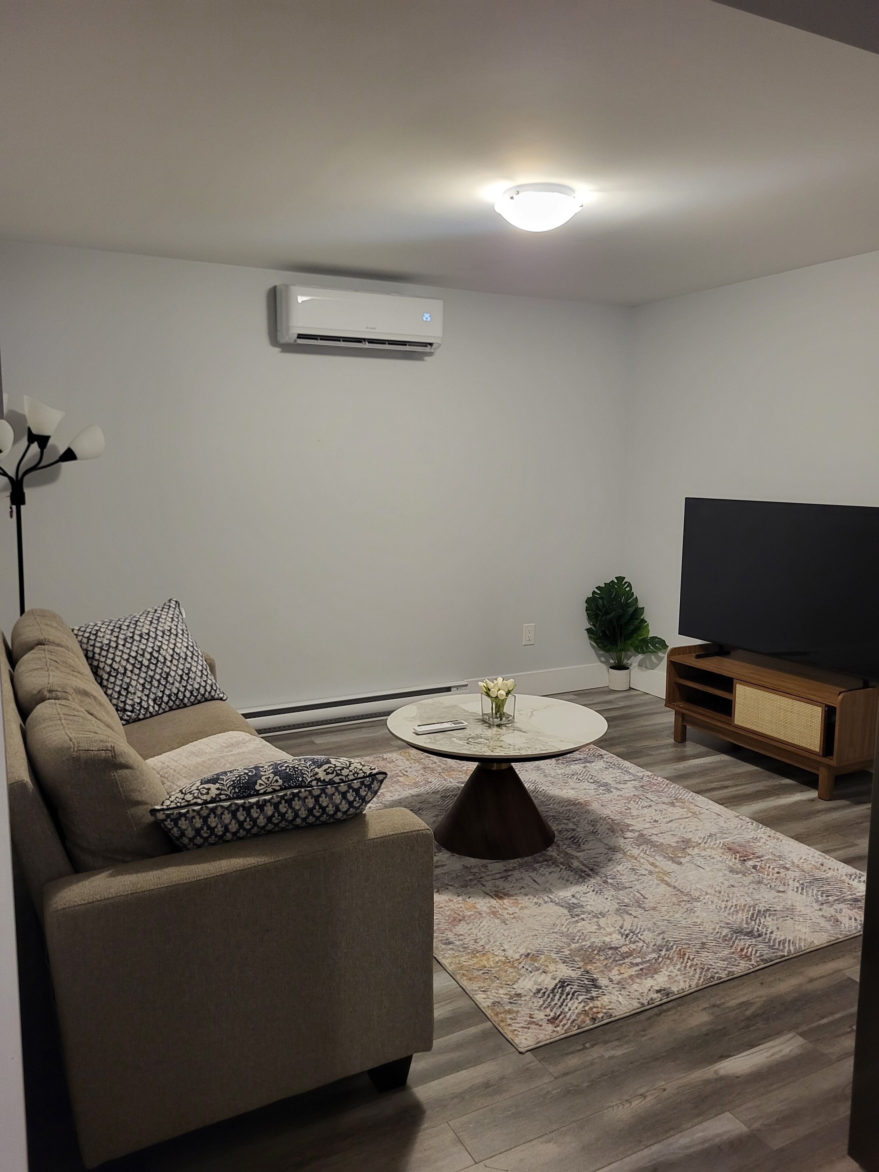 Een woonkamer met een bank, een salontafel, een tv-meubel en een airconditioner.