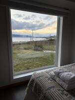 Un dormitorio con un amplio ventanal que da a una zona verde y un cuerpo de agua.