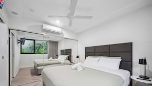 Habitación de hotel moderna con una cama grande, una cama más pequeña, un ventilador de techo, un televisor y una ventana con vistas a zonas verdes.